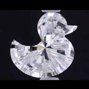 May include: A clear, faceted crystal duck figurine with a detailed, multi-faceted design. The duck is set against a black background, showcasing its brilliant, reflective surfaces. The duck's form is clearly defined, with a beak and rounded body.