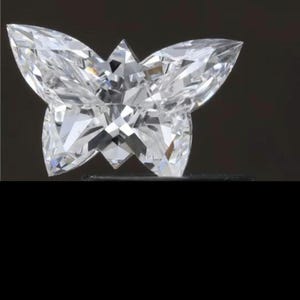 May include: A clear, faceted gemstone shaped like a butterfly. The butterfly has pointed wings and a detailed, multi-faceted surface, reflecting light. The gemstone is set against a dark background, highlighting its brilliance and form.
