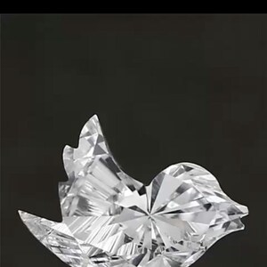 May include: A faceted, clear crystal bird sculpture with a detailed, geometric design. The sculpture is positioned against a black background, showcasing its intricate cuts and reflective surfaces. The bird's form is stylized and elegant.