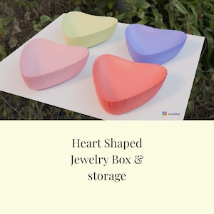 Könnte beinhalten: Vier herzförmige Aufbewahrungsboxen in Pastellfarben: Rosa, Gelb, Lila und Koralle. Jede Box hat eine geriffelte Außenseite und steht auf einer weißen Oberfläche. Der Text "Heart Shaped Jewelry Box & storage" ist enthalten.