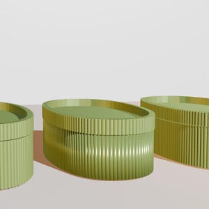 Può includere: Tre scatole decorative verde oliva di varie dimensioni. Le scatole hanno una texture a coste sui lati e un coperchio liscio e piatto. Le scatole sono disposte su una superficie di colore chiaro.