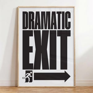 May include: A framed art print with the words "DRAMATIC EXIT" in bold black letters. Below the text is a black graphic of a person running towards an arrow, indicating an exit. The print is in a light wood frame.
