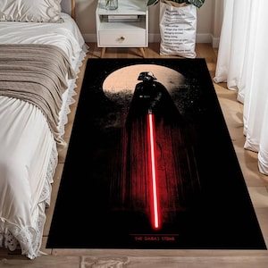 Puede incluir: Alfombra rectangular negra con Darth Vader con un sable de luz rojo sobre un fondo de luna. La alfombra tiene el texto "THE DARK SIDE" en la parte inferior. La alfombra est&aacute; sobre un suelo de madera.
