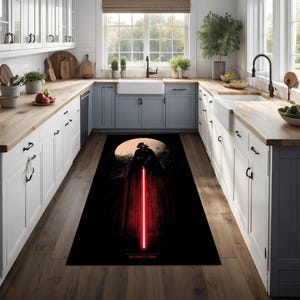 Puede incluir: Alfombra rectangular negra con Darth Vader y un sable de luz rojo sobre un fondo de luna. La alfombra tiene el texto "THE DARK SIDE" en la parte inferior. La alfombra est&aacute; colocada en una cocina con armarios blancos y encimeras de madera.