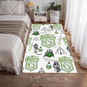 Puede incluir: Alfombra rectangular blanca con un patrón repetido de escudos verdes de Slytherin, calaveras, botellas de pociones y símbolos de las Reliquias de la Muerte. La alfombra tiene texto que dice "Slytherin", "Crucio" y "The boy who lived, Come to die".