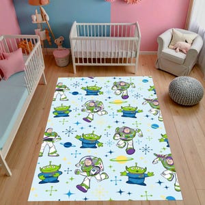 Könnte beinhalten: Ein hellblauer rechteckiger Teppich mit einem sich wiederholenden Muster der Zeichentrickfiguren Buzz Lightyear und die kleinen grünen Männchen aus Toy Story. Der Teppich hat einen hellblauen Hintergrund mit Planeten und Sternen.