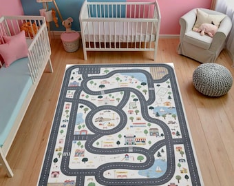 Puede incluir: Una alfombra de juego rectangular con un diseño de mapa de carreteras. La alfombra presenta carreteras grises que serpentean a través de una ciudad con casas, árboles y un lago. La alfombra está sobre un piso de madera en una habitación infantil.