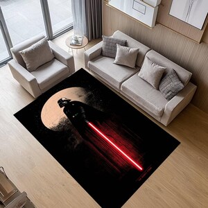 Puede incluir: Alfombra rectangular negra con Darth Vader con un sable de luz rojo sobre un fondo de luna y estrellas. La alfombra tiene un tema de Star Wars y est&aacute; colocada en un sal&oacute;n.