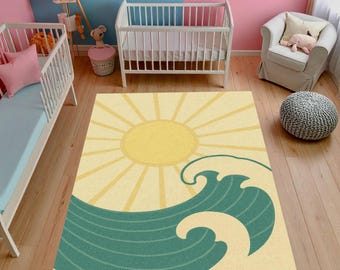 May include: A rectangular rug with a yellow sun and teal waves design. The rug is placed on a wooden floor in a nursery setting, with two cribs and a chair visible in the background. The rug's design evokes a beach or ocean theme.