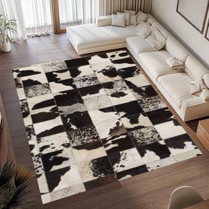 May include: A large, rectangular cowhide rug with a patchwork design. The rug features a pattern of black and white squares, creating a bold, geometric look. The rug is placed on a hardwood floor, and a white sofa is in the background.