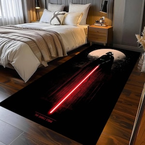Puede incluir: Alfombra rectangular negra con un gr&aacute;fico de Darth Vader y un sable de luz rojo. Una gran luna blanca est&aacute; en el fondo. El texto "THE DARK SIDE" est&aacute; en la parte inferior.