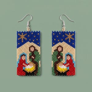 Op de afbeelding: Een paar rechthoekige kralenoorbellen met een kerststalscène met figuren in rode, groene en bruine gewaden. Het ontwerp bevat een felgeel centrum, een beige achtergrond en een donkerblauwe sterrenhemel met een gouden ster.