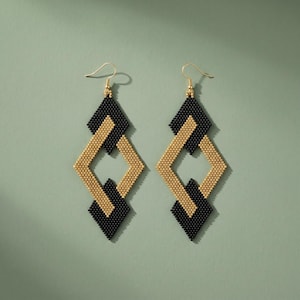 Peut inclure: Boucles d'oreilles pendantes géométriques avec un motif de perles dorées et noires. Les boucles d'oreilles présentent une forme de losange avec un centre doré et des accents noirs, suspendues à des crochets dorés. Un accessoire élégant.
