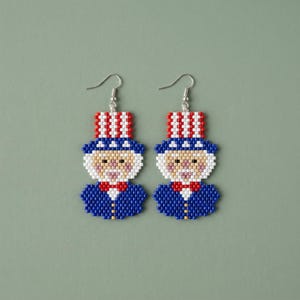 May include: A pair of beaded Uncle Sam earrings. Each earring features a blue jacket, a white face, a red bow tie, and a red, white, and blue top hat. The earrings hang from silver-colored fish hook ear wires.
