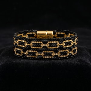 May include: A beaded bracelet with a gold chain link design on a black background. The bracelet features a gold magnetic clasp. The bracelet is made of small black and gold beads.