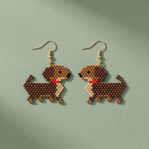 Può includere: Un paio di orecchini pendenti con motivo a bassotto, realizzati con piccole perline marroni, beige e nere. Ogni cane ha un collare rosso brillante ed è appeso a un gancio in metallo dorato. Il design ha un aspetto pixelato.