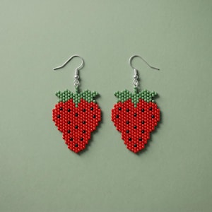May include: A pair of strawberry-shaped dangle earrings crafted from small red, green, and black beads. Each earring features a red body with black seed accents and a green leafy top, suspended from a silver-toned metal hook for pierced ears.