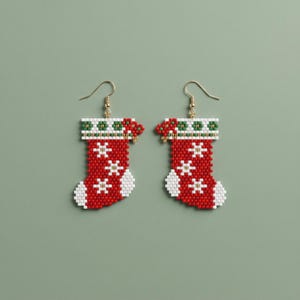 Peut inclure: Une paire de boucles d'oreilles pendantes en perles en forme de chaussettes de Noël. Les chaussettes sont principalement rouges avec des motifs de flocons blancs, un bout et un talon blancs, et un revers à motifs verts et blancs.