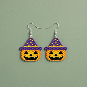 May include: A pair of beaded drop earrings featuring a jack-o'-lantern pumpkin design with a bright orange face, black eyes and mouth, and a purple witch hat with yellow polka dots, suspended from silver-toned metal fishhook ear wires.