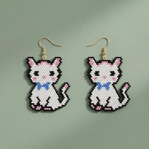 May include: A pair of cat-shaped earrings. Each earring features a white cat design with black outlines, pink accents, and a blue bow tie. The earrings have gold-colored hooks.