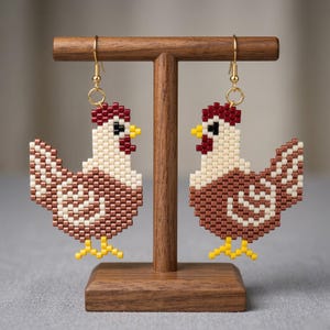 May include: A pair of beaded chicken earrings. The earrings are brown, white, and red, with yellow feet and gold-colored hooks. The earrings are displayed on a wooden jewelry stand.