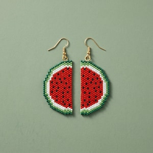May include: A pair of dangle earrings crafted from small beads in the shape of watermelon slices. Each earring features a red center with black seed details, a white rind, and a green outer edge, suspended from gold-toned metal ear wires.