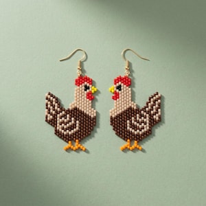 Pode incluir: Um par de brincos pendentes com um design de galinha feito de missangas. Cada galinha é composta por pequenas missangas em tons de castanho, creme, vermelho e amarelo, com um gancho de metal dourado. As figuras estão viradas uma para a outra.