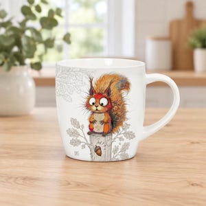 May include: A white ceramic mug featuring a colourful illustration of a squirrel with large eyes sitting on a tree stump. The design includes grey line drawings of oak leaves and branches, with a single brown acorn depicted below the squirrel.