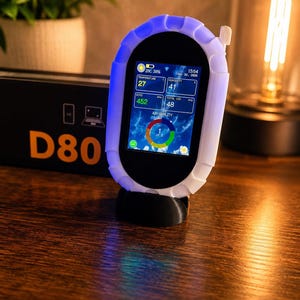 Könnte beinhalten: Ein D80 Luftqualitätsmonitor mit einem weißen, texturierten, ovalen Schutzgehäuse und einem schwarzen Ständer. Der digitale Bildschirm zeigt Temperatur, Luftfeuchtigkeit, CO2, VOC-Gesamtwerte und eine kreisförmige Luftqualitätsanzeige mit dem Text 1 of 5.