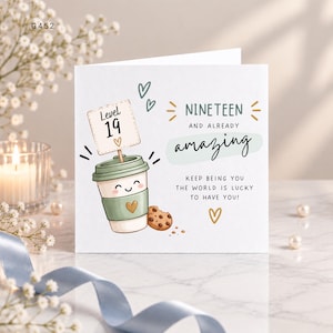 May include: A square greeting card featuring a cartoon coffee cup with a smiling face, a chocolate chip cookie, and a sign that says Level 19. The text reads NINETEEN AND ALREADY amazing, KEEP BEING YOU THE WORLD IS LUCKY TO HAVE YOU! with heart icons.
