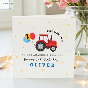May include: A white square greeting card featuring a red tractor illustration pulling a blue, yellow, and red balloon cluster. The card includes the text BEEP BEEP! I'M 2!, TO OUR AMAZING LITTLE BOY, Happy 2nd Birthday, and the name OLIVER in blue.