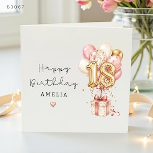 May include: A white square birthday greeting card featuring the text Happy Birthday AMELIA with a small heart icon. The design includes a cluster of pink, white, and gold balloons, gold number 18 balloons, and a gift box tied with a pink ribbon.