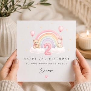 May include: A square birthday greeting card featuring a watercolor illustration of a teddy bear and a bunny sitting on clouds with a pastel rainbow and a pink number two. The text reads HAPPY 2ND BIRTHDAY TO OUR WONDERFUL NIECE and Emma.
