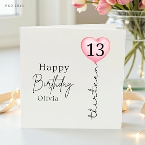 Pode incluir: Um cartão de aniversário quadrado branco com o texto preto Happy Birthday Olivia. Um gráfico de balão rosa em forma de coração está posicionado à direita com o número 13 em preto e a palavra thirteen escrita verticalmente abaixo.