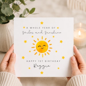 May include: A square white greeting card featuring a yellow sun illustration with a smiling face, surrounded by small yellow stars. The text reads: A WHOLE YEAR OF Smiles and Sunshine HAPPY 1ST BIRTHDAY Reggie. The code RSD 2137 is at the top.