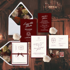 Könnte beinhalten: Hochzeitseinladungs-Set mit bordeauxroten und cremefarbenen Papeterie-Elementen. Das Set umfasst eine "Save the Date"-Karte, eine Einladung, eine Detailkarte und eine RSVP-Karte. Weiße Umschläge und florale Akzente ergänzen das Design. Eine kleine Ringbox und Briefmarken sind ebenfalls enthalten.