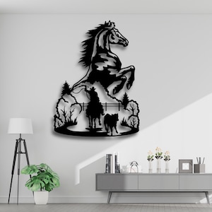 May include: Black metal wall art depicting a rearing horse above a scene with a cowboy on horseback, a dog, and trees. The artwork is a silhouette, creating a dramatic contrast against the white wall. The horse is the focal point.