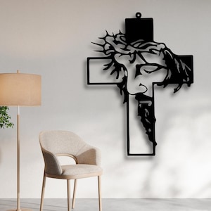 May include: Black metal wall art depicting Jesus on a cross, with a crown of thorns. The artwork features a detailed silhouette of Jesus's face and beard. The cross has a loop at the top for hanging. A religious themed home decor item.