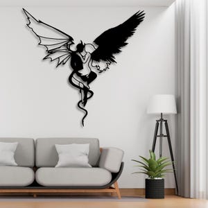 May include: A black metal wall art piece depicting a devil and an angel embracing, with one side featuring a devil with horns and the other an angel with wings. The artwork is mounted on a white wall above a gray sofa.
