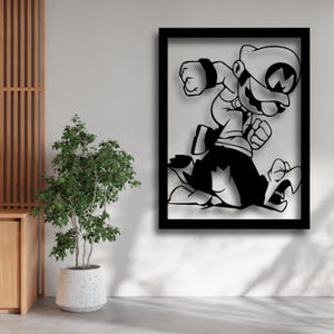 May include: Black metal wall art of a cartoon character in a running pose, framed in a black rectangular frame. The character is wearing a hat and overalls. The artwork is displayed on a white wall next to a potted plant.