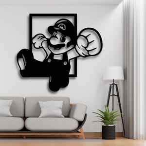 Peut inclure: Décoration murale en métal noir représentant le personnage Mario du jeu vidéo Super Mario Bros. L'œuvre représente Mario dans une pose dynamique, encadrée dans un carré noir. L'art est monté sur un mur blanc.