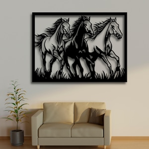 Könnte beinhalten: Schwarze Metall-Wandkunst mit drei galoppierenden Pferden. Die Pferde sind als Silhouette dargestellt, mit wehenden Mähnen und Schweifen, vor einem neutralen Hintergrund. Das Kunstwerk ist in einem schwarzen Rahmen eingefasst und hat eine grasbewachsene Basis.