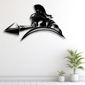 Puede incluir: Arte mural de metal negro que representa a un guerrero espartano con casco y lanza. La obra de arte está montada en una pared blanca sobre un suelo blanco y plantas en macetas. El guerrero está en una pose dinámica.