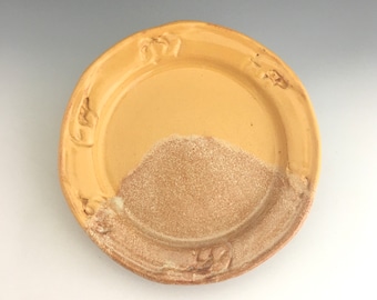 May include: A yellow ceramic plate with a raised rim and a textured design. The plate has a light brown glaze on the bottom half.