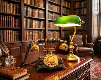 May include: A vintage-style rotary telephone with a black and gold finish sits on a wooden desk next to a brass banker's lamp with a green glass shade. A stack of leather-bound books and a glass inkwell with a quill pen are also present.