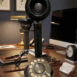 Könnte beinhalten: Ein schwarzes Vintage-Stabtelefon mit einer kreisförmigen Wählscheibe mit weißen Ziffern an der Basis, einem hohen vertikalen Schaft und einem großen, oben montierten runden Hörer, der über ein schwarzes Kabel mit dem Hauptgehäuse verbunden ist.