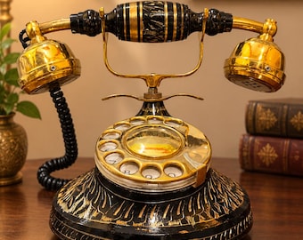 May include: A rotary telephone featuring a black base and handset with intricate gold-colored hand-painted detailing. The device includes a gold-finished rotary dial, a central circular emblem, and a black coiled cord connecting the handset to the base.