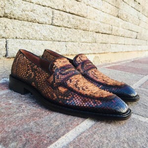 May include: A pair of brown and black leather loafers with a snakeskin pattern. The shoes have a classic slip-on design with a low heel and a rounded toe. The leather has a textured appearance.