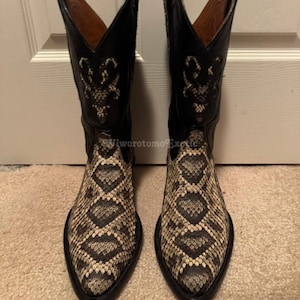 May include: A pair of cowboy boots featuring a snakeskin pattern on the foot and black leather uppers. The boots have pointed toes and decorative stitching on the shaft. The boots are made of leather and are designed for wear.