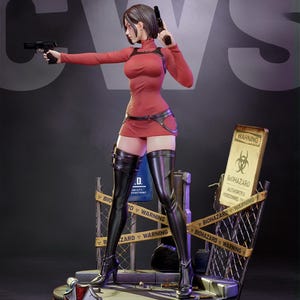 May include: A detailed figurine of a character in a red dress, holding two black pistols. The figure is wearing black thigh-high boots and a harness. The base features a biohazard warning sign and the text "BIOHAZARD WARNING".